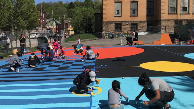 Photograph of children and community members painting a large mural on the ground
