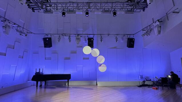 Room with blue lighting and spotlighting set up with standing piano and other equipment.