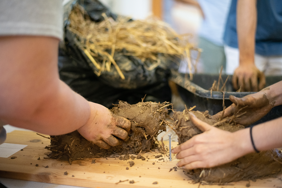 Close-up of people handling mud and straw construction materials
